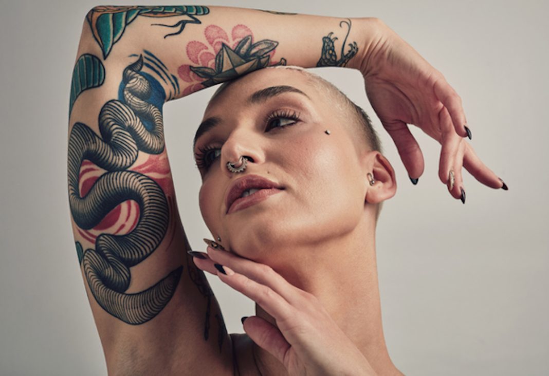 Woman, natural beauty and tattoo with skin, dermatology and wellness in studio for glow on white background. Skincare, face and body art with piercing, edgy and trendy for fashion and cosmetics